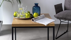 Una habitación moderna con una mesa de madera, estructura metálica, un jarrón azul, una silla gris y una planta en maceta.