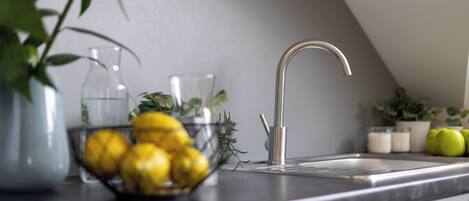 A kitchen with a modern sink, a bowl of lemons, and a potted plant.