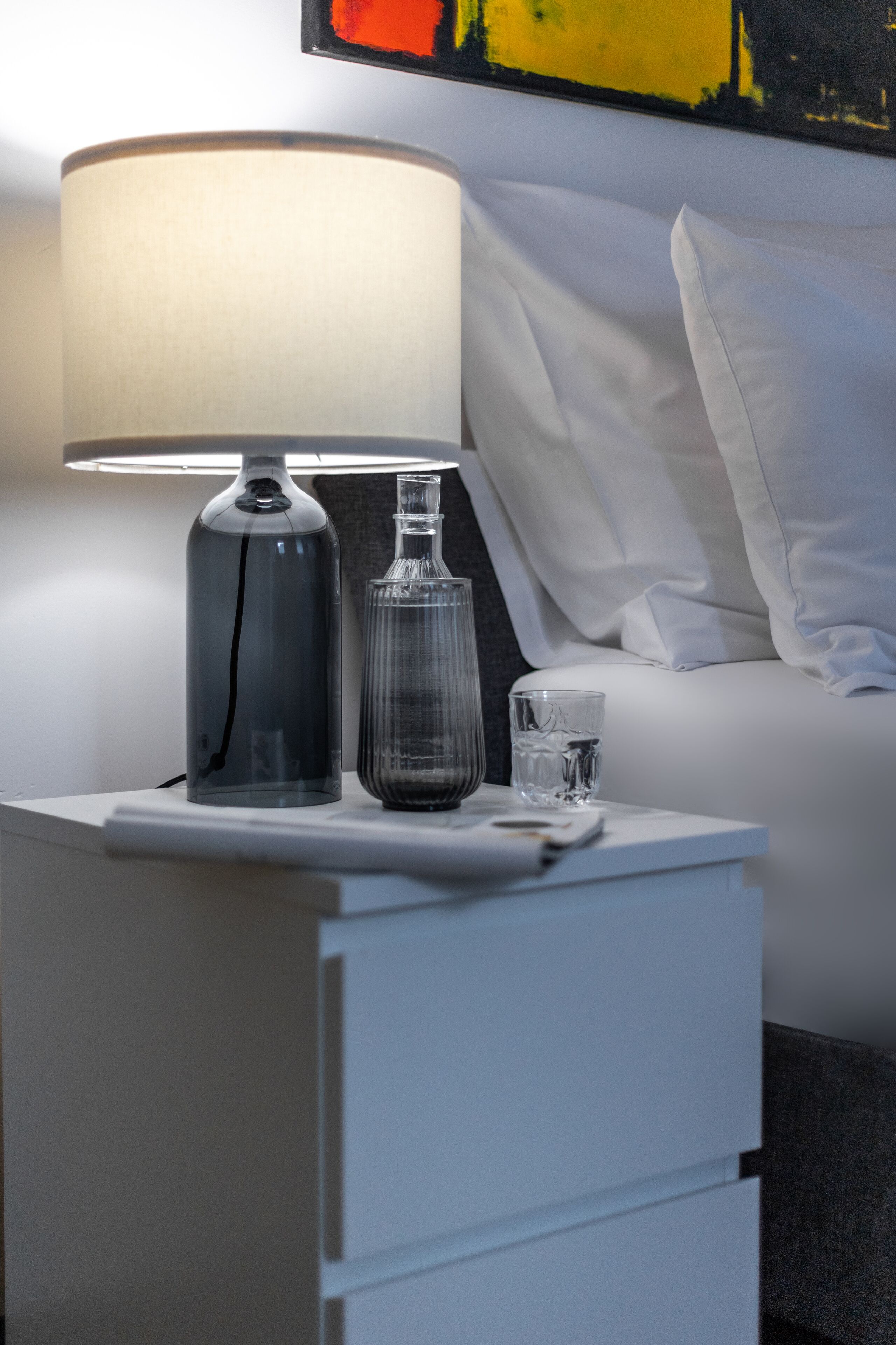 Een netjes opgeruimd nachtkastje met een lamp, een glazen fles en een glas water.