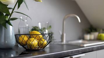 Uma bancada de cozinha com uma cesta de arame contendo limões, um vaso com flores brancas e um jarro de vidro.