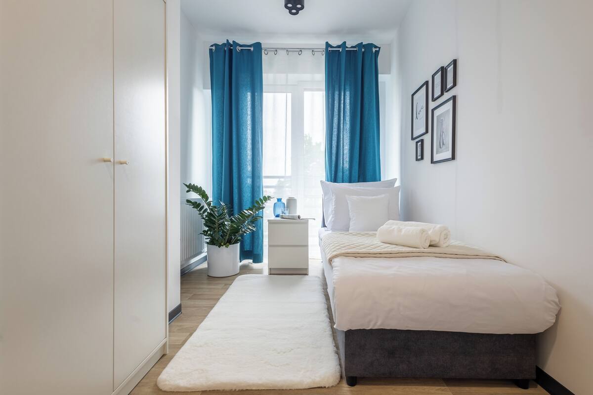Un dormitorio con cama, mesita de noche, cortinas y decoración en la pared.