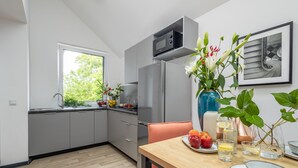 Una cocina moderna con gabinetes grises, un refrigerador de acero inoxidable, un microondas y un comedor con una mesa y sillas de madera.