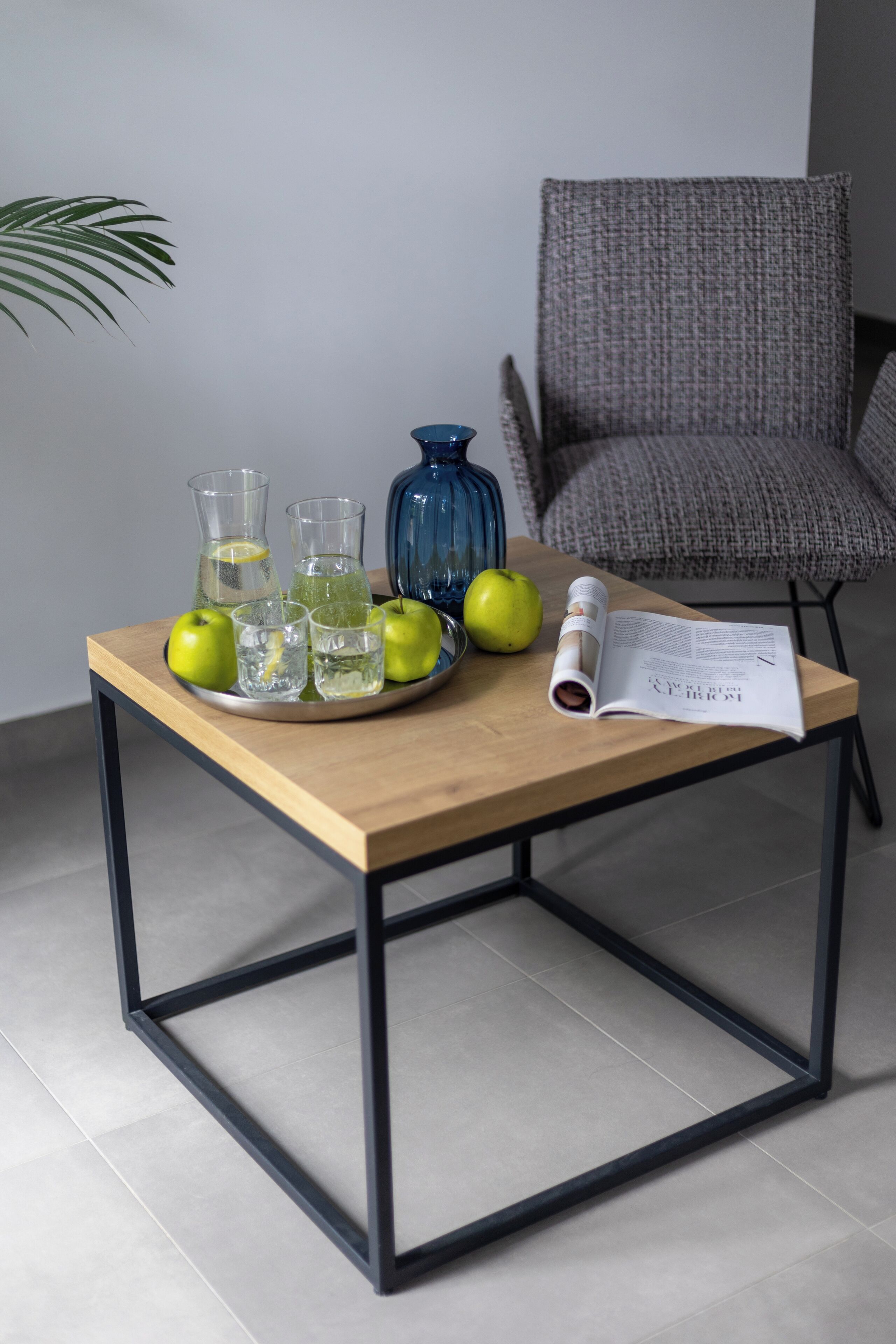 A wooden table with a glass pitcher, two glasses, and two apples.