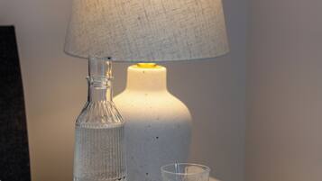 A white table with a clear glass bottle, a glass, and a lamp with a white shade.