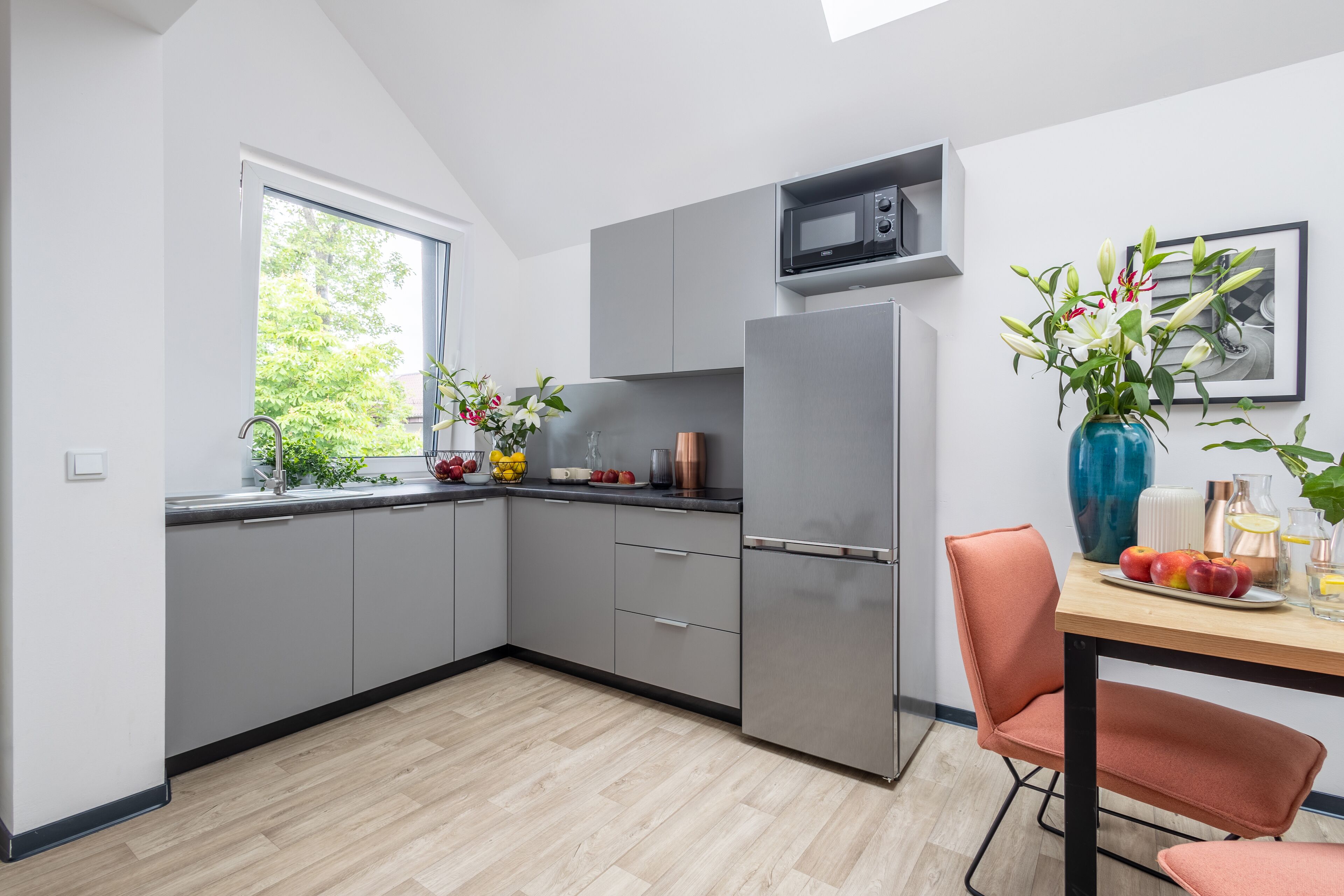 A modern kitchen with grey cabinets, a stainless steel refrigerator, a microwave, and a dining area with a table and chairs.