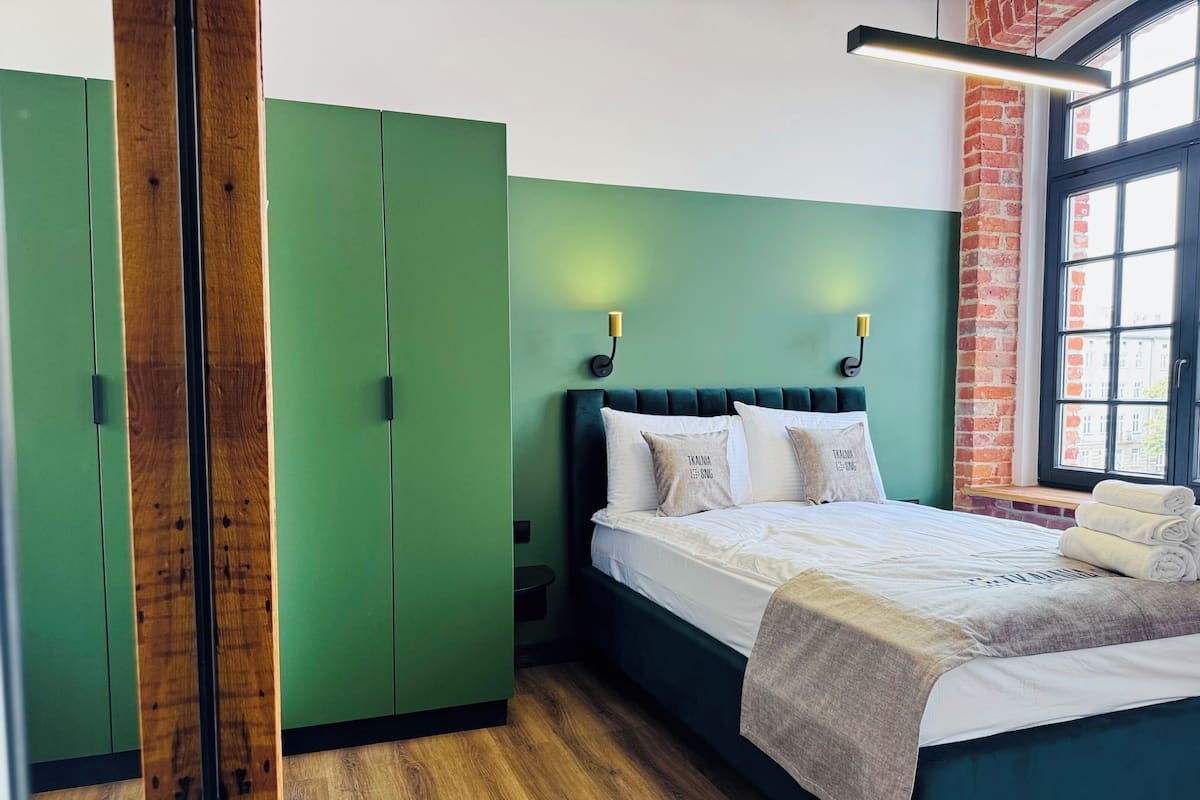 Un dormitorio con un armario verde, una cama con ropa de cama blanca y una pared de ladrillo.