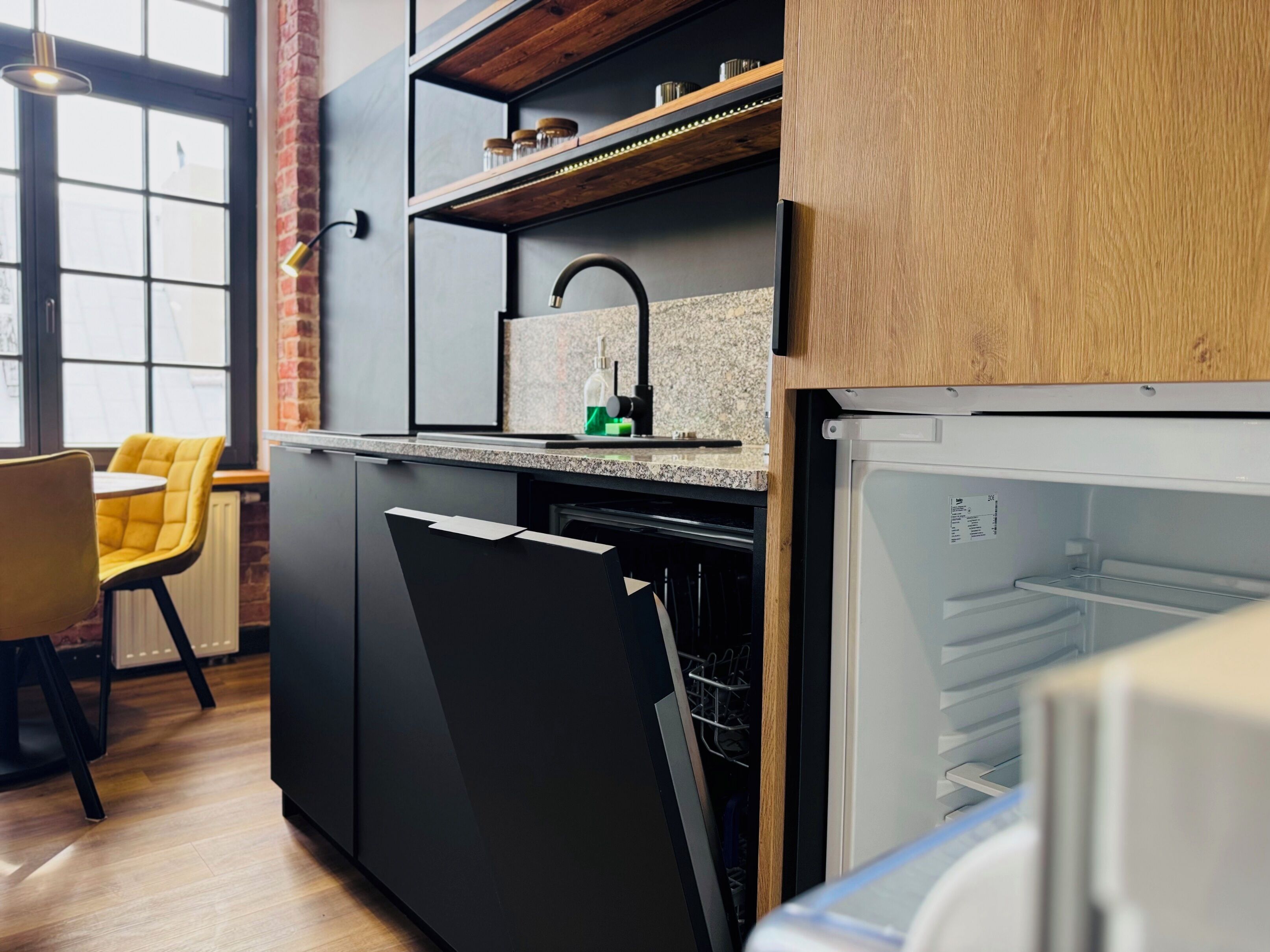 A modern kitchen with a built-in dishwasher, a granite countertop, and a wooden shelf above the sink.