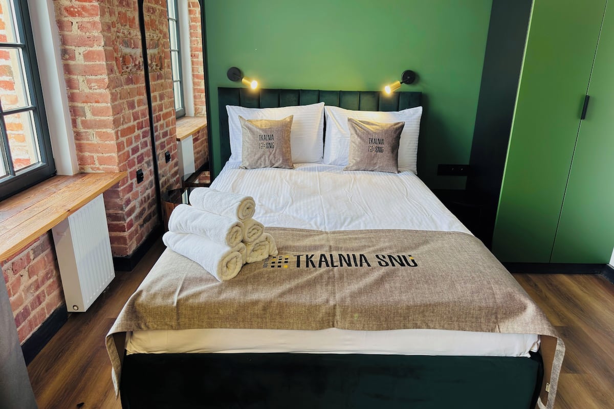 Una cama bien hecha con una toalla, una pared verde y una pared de ladrillo.