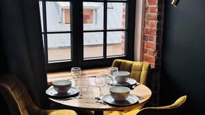 A dining table with four chairs, a window with a view of buildings, and a brick wall. - Tkalnia Snu (Lódz)