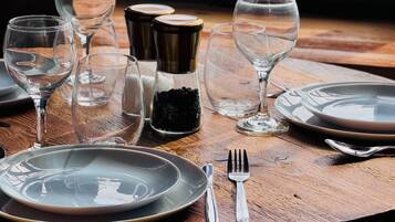 Una mesa de madera dispuesta con platos, cubiertos y copas de vino vacías.