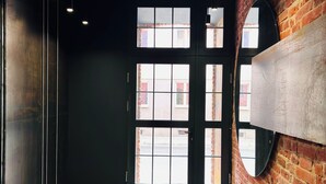 A hallway with a brick wall, a large door with multiple windows, and a tiled floor. - Tkalnia Snu (Lódz)