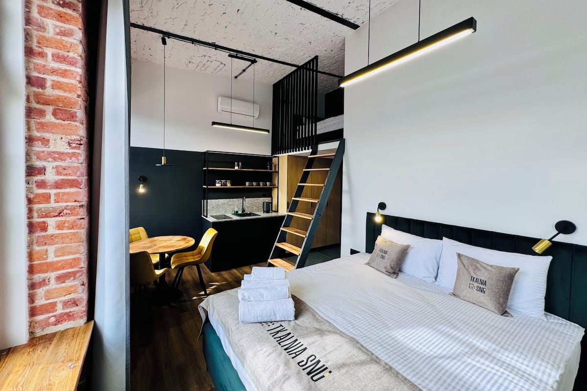 Un dormitorio moderno con cama, un escritorio pequeño y una silla. Una escalera conduce a una zona superior.