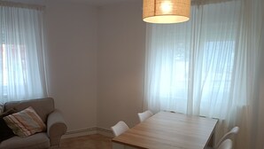 A room with a wooden dining table, white chairs, a beige sofa, and sheer curtains. - Comfortable apartment in Oviedo (Oviedo)