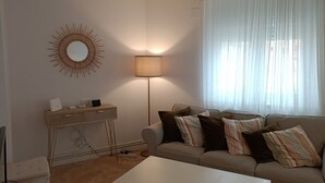 A living room with a sofa, a coffee table, a lamp, a desk with a mirror, and a window with sheer curtains. - Comfortable apartment in Oviedo (Oviedo)
