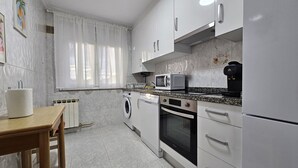 A modern kitchen with white cabinets, a built-in microwave, a coffee maker, a washing machine, and a dining area with a wooden table and chairs. - Comfortable apartment in Oviedo (Oviedo)