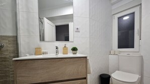 A modern bathroom with a wooden vanity, a mirror, a toilet, and a window. - Comfortable apartment in Oviedo (Oviedo)