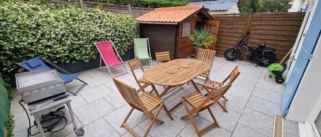 Un patio con una mesa y sillas de madera redondas, una parrilla, una silla plegable y un cobertizo pequeño.