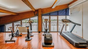 A gym with exercise equipment, large windows, and wooden beams. - Hotiday Grado Marina (Grado)