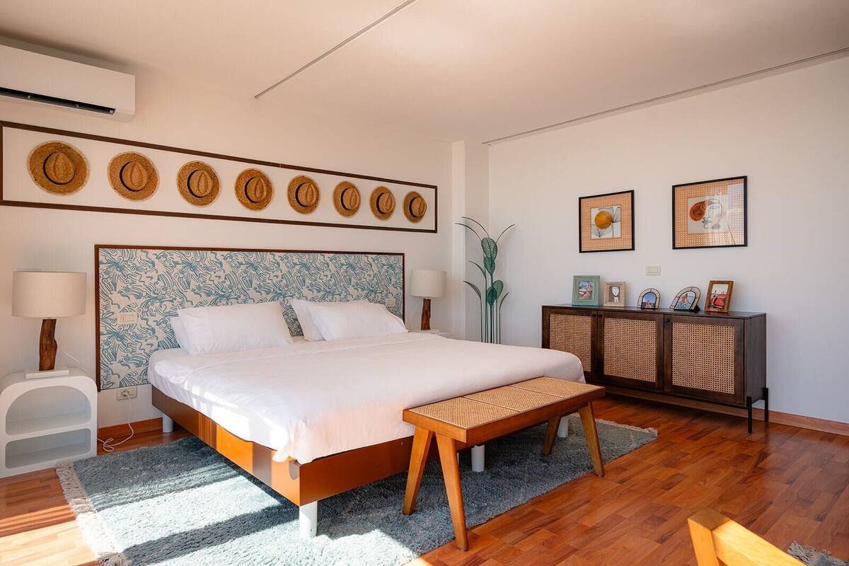 A modern bedroom with a large bed, bedside tables, a bench, a console table with pictures, and a wall with circular decorations.