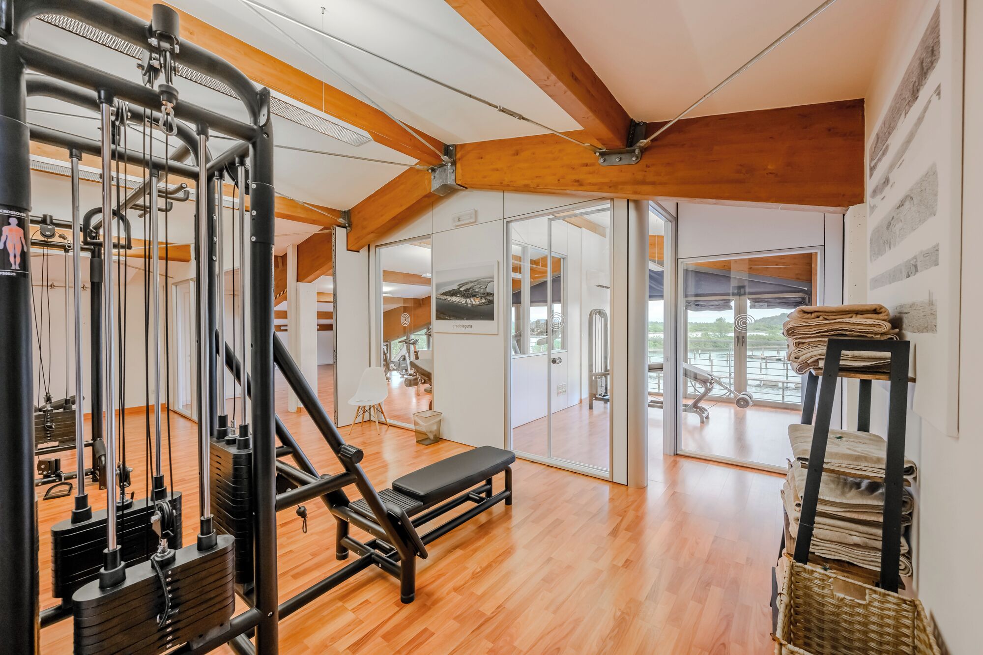 Ein Fitnessraum mit Trainingsgeräten, Holzböden und Blick auf ein Gewässer.