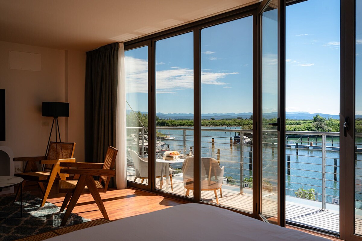 A hotel room with a large sliding glass door leading to a balcony with a view of a body of water and boats.