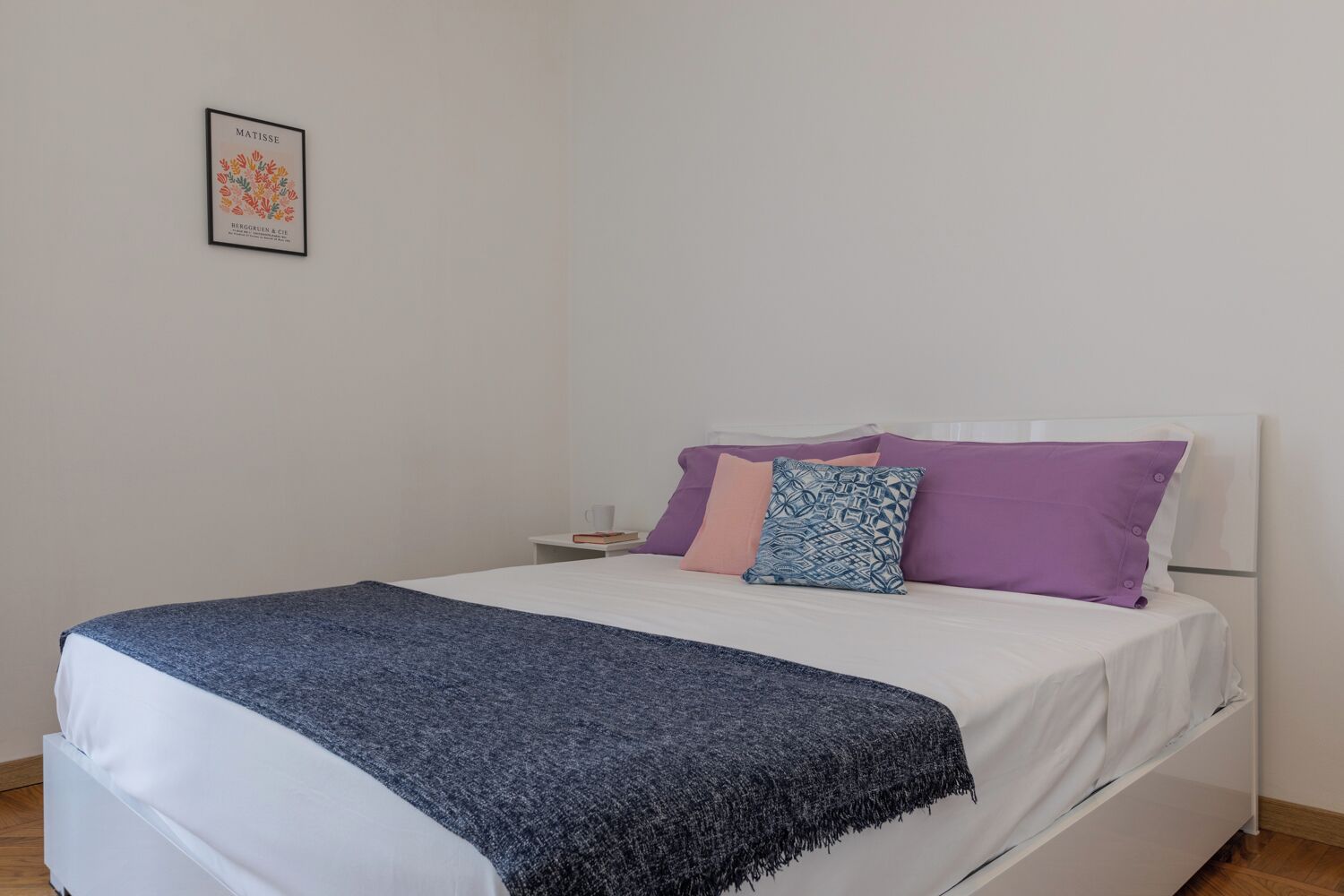 A neatly made bed with a blue blanket and multiple pillows in purple and blue.