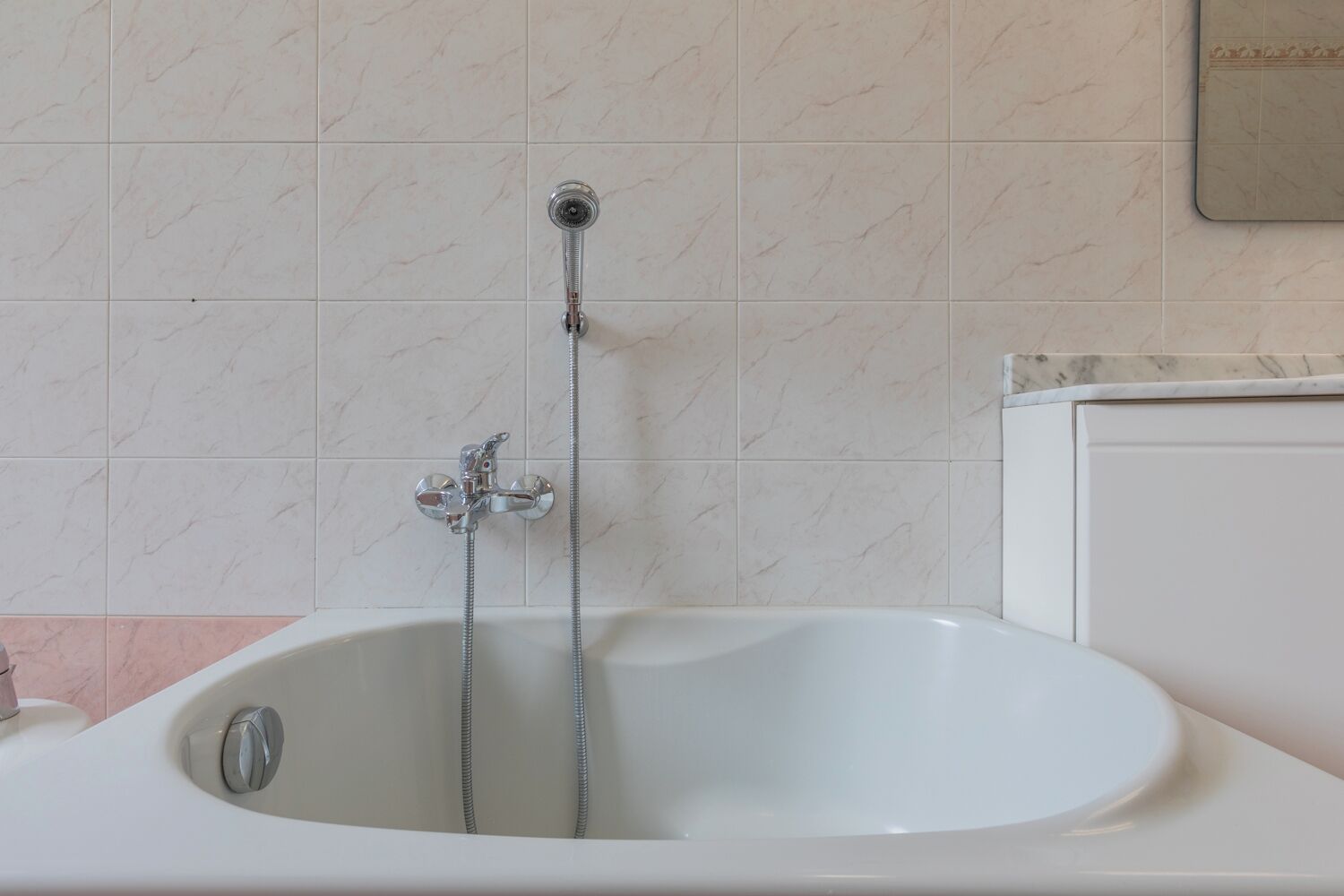 A bathroom with a white bathtub, a showerhead, and a toilet.