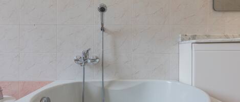 A bathroom with a white bathtub, a showerhead, and a toilet.
