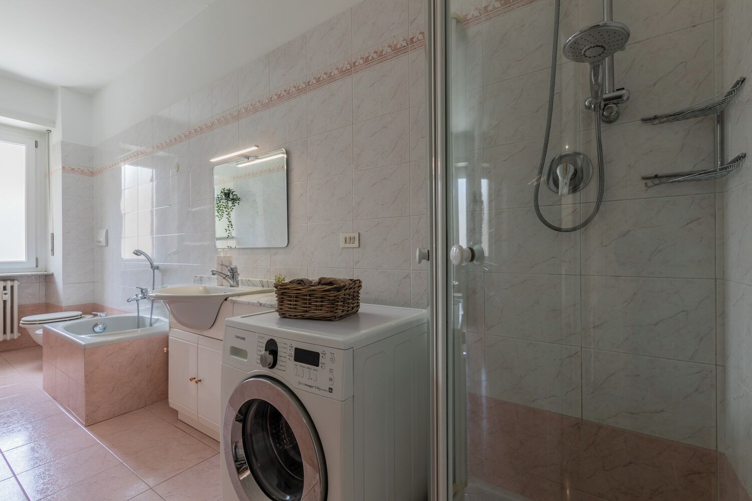 A modern bathroom with a washing machine, a sink, a shower, and a glass-enclosed shower area.