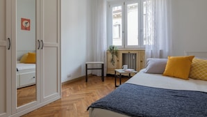 A bedroom with a bed, a bedside table, a chair, a radiator, and a window with curtains. - Casa Gabri by Wonderful Italy (Turin)