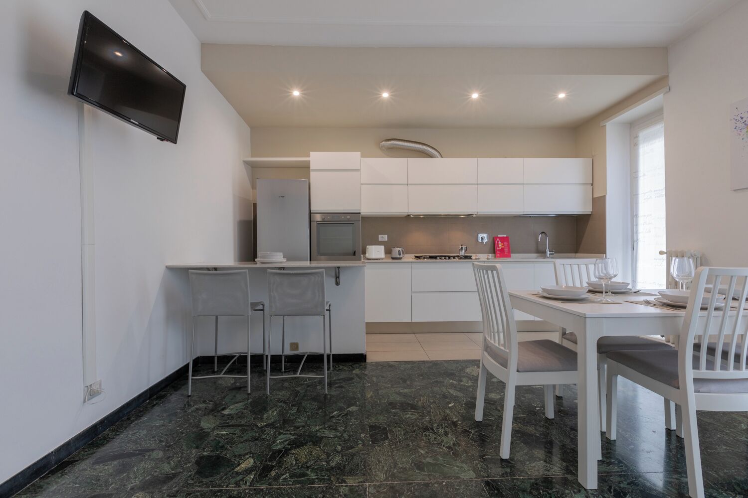 A modern kitchen with white cabinets, a built-in oven, and a dining area with a table and chairs.