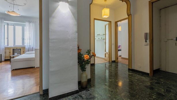 A hotel hallway with a bed, a vase of flowers, and a mirror. - Casa Gabri by Wonderful Italy (Turin)