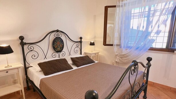 A neatly made bed with a headboard, two bedside tables with lamps, a decorative wall piece, and a window with a sheer curtain.
