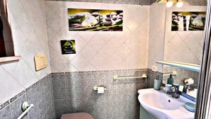 A bathroom with a toilet, sink, and mirror. There are decorative tiles and a small picture frame on the wall.