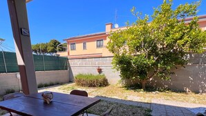 An outdoor patio with a table and chairs, a small tree, and a building in the background.