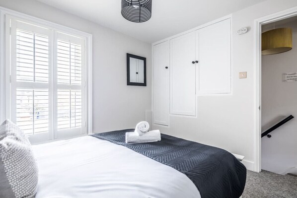 A bedroom with a bed, a window with blinds, a door, and a small wall-mounted shelf.