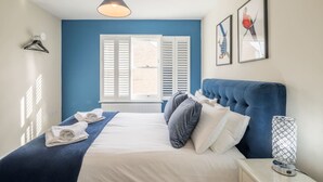 A bedroom with a bed, a hanging light, a window with shutters, and a wall-mounted lamp. - Beautiful 2bed Central Home (Cambridge)