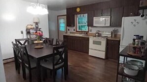 A compact kitchen with dark wooden cabinets, a white refrigerator, and a dining area with a table and chairs.