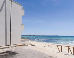 Una propiedad frente a la playa con un edificio blanco, una playa arenosa y un cielo azul despejado.