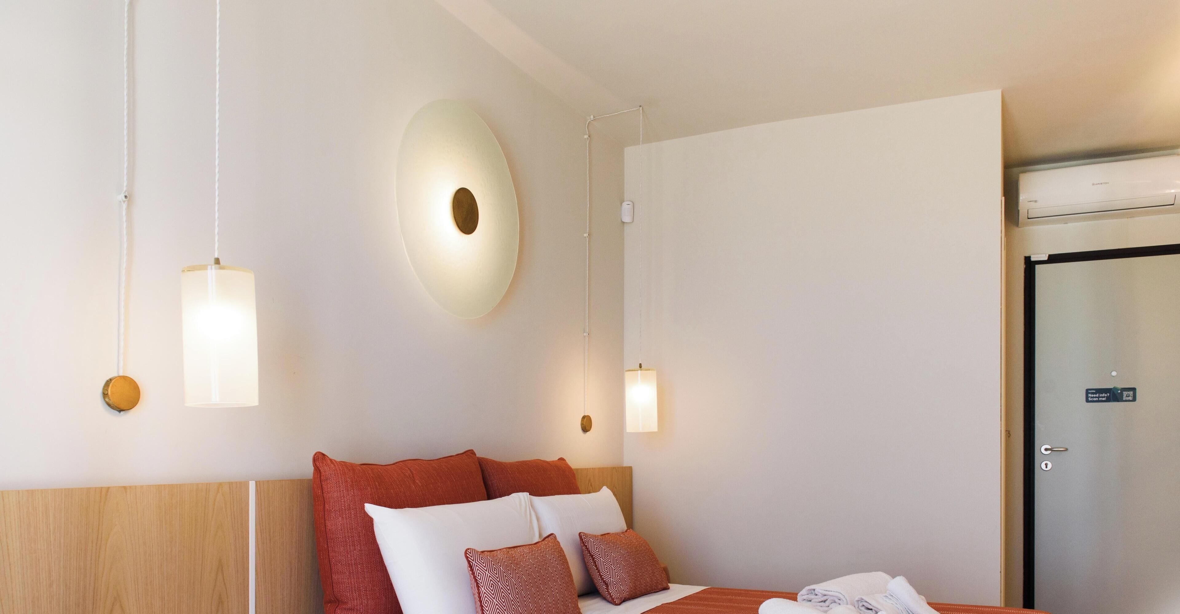 Une chambre d’hôtel avec un lit, un luminaire fixé au mur et une porte.