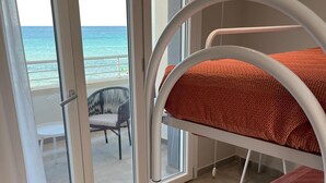 Een balkon met uitzicht op de oceaan, een wit metalen stapelbed en een witte stoel.