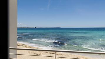 Une vue sur la plage depuis un balcon doté d’une balustrade, avec un ciel dégagé et une mer calme.