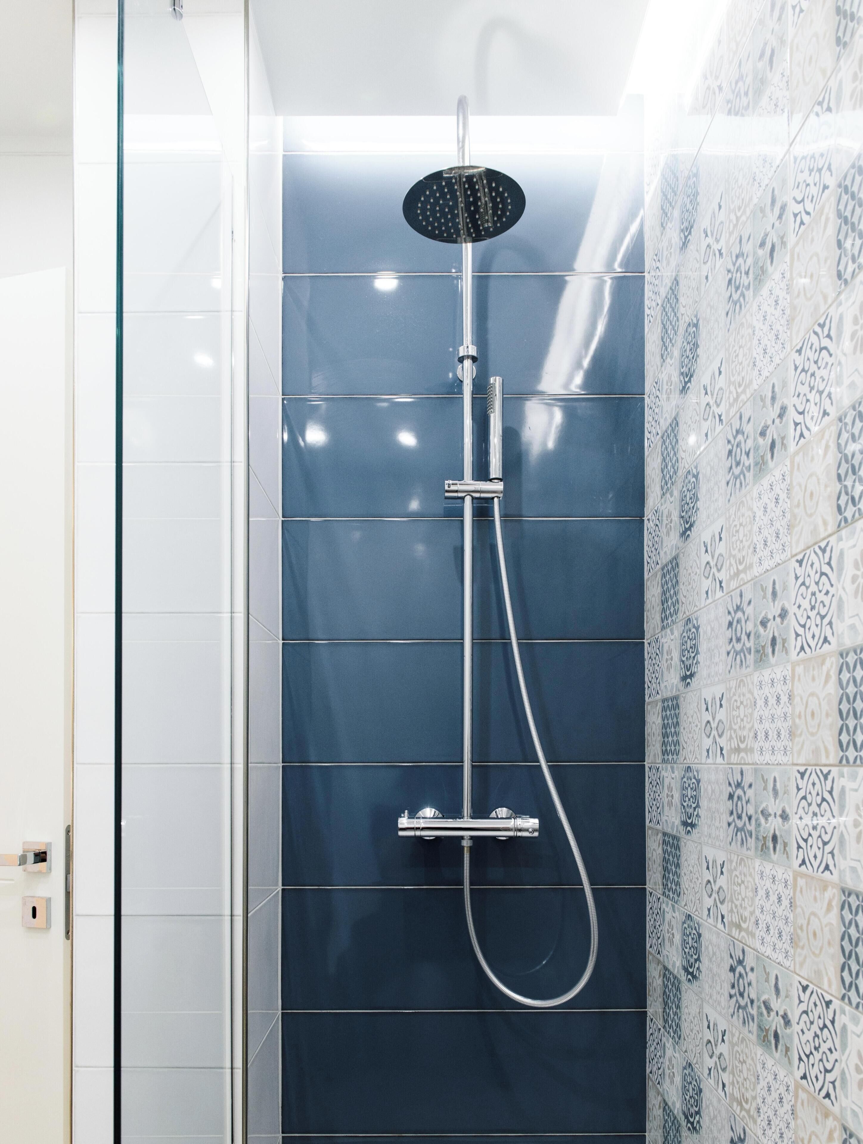 A shower with a handheld showerhead and a wall-mounted control panel.