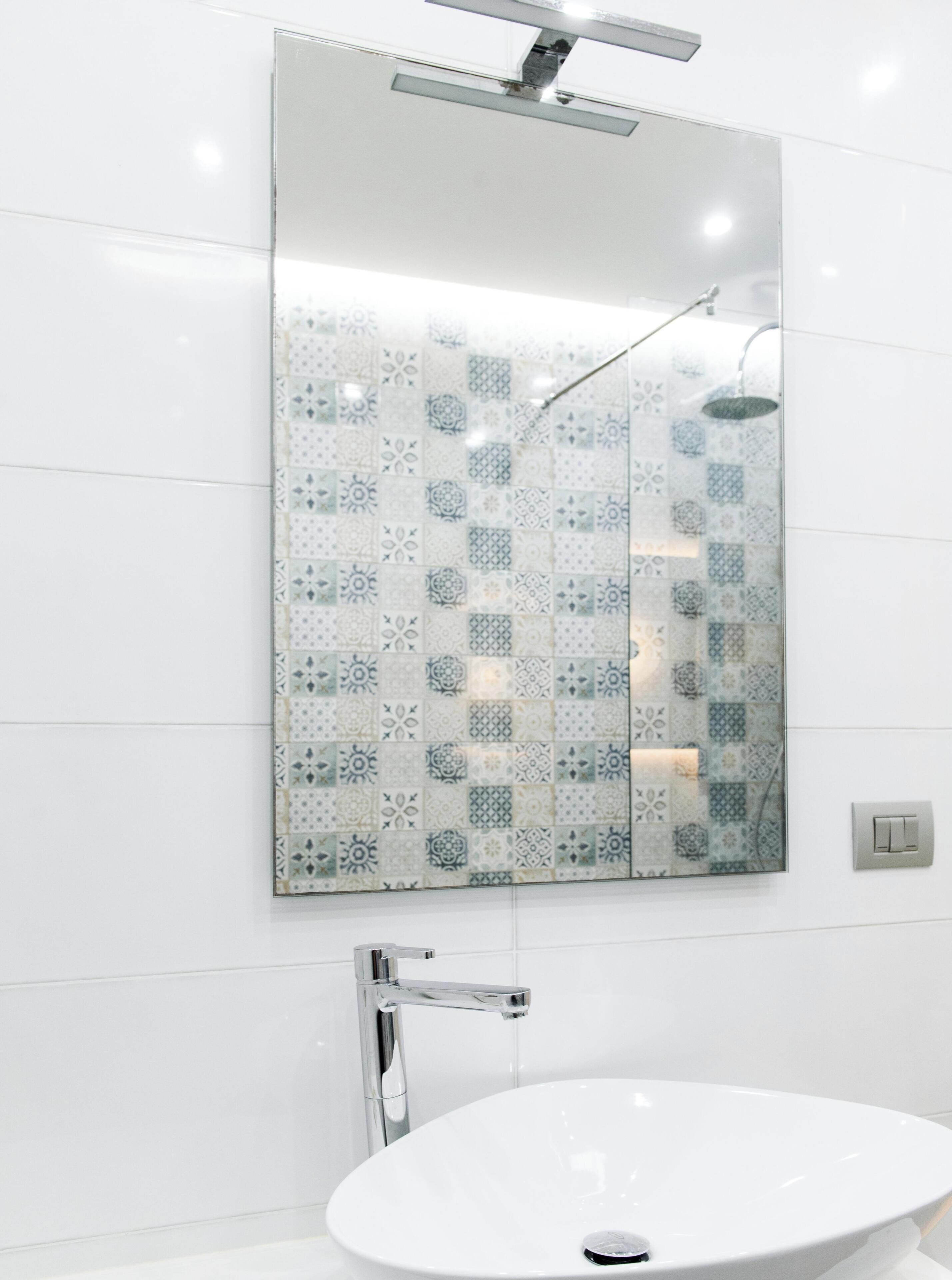 Ein Badezimmer mit einem weißen Waschbecken, einer Dusche mit Glastür und einer Wand mit gemusterten Fliesen.