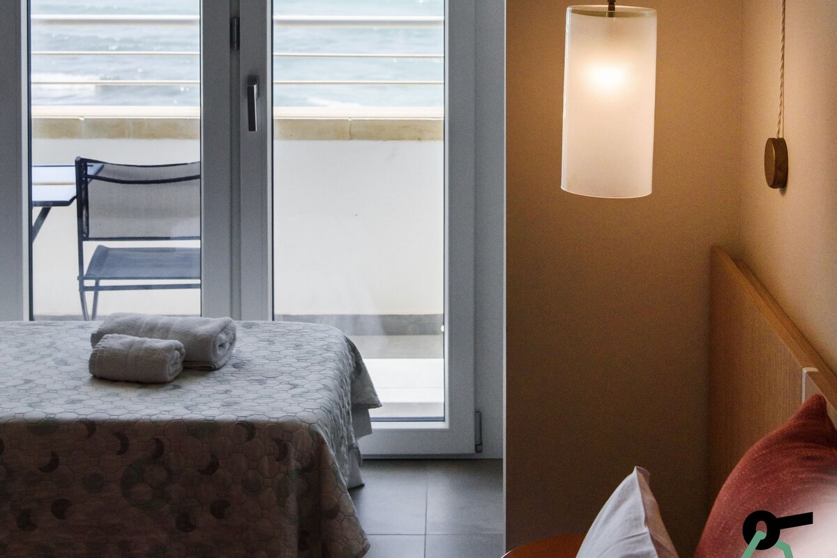 Un dormitorio con cama, una silla, una mesita de noche y una lámpara colgante.