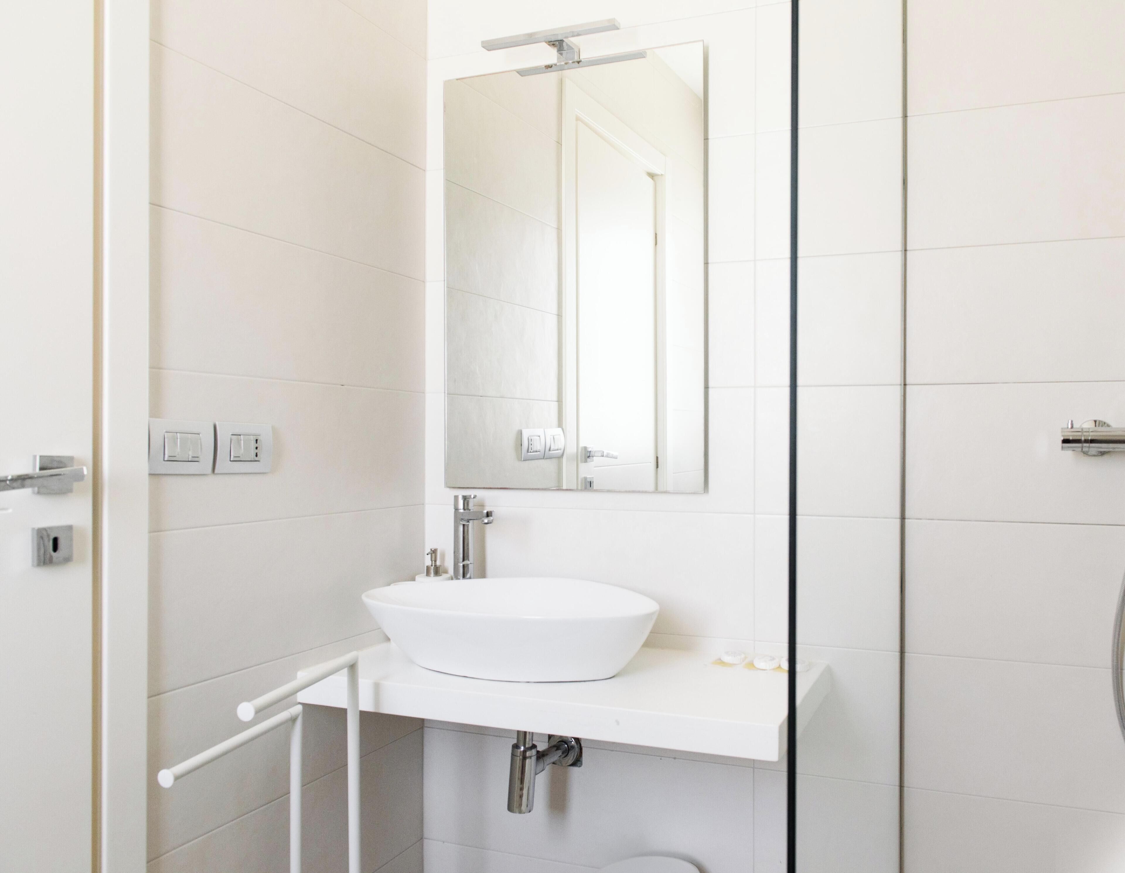 Un baño moderno con un lavamanos blanco, un espejo y una zona de ducha.