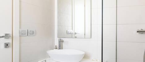 Un baño moderno con un lavamanos blanco, un espejo y una zona de ducha.