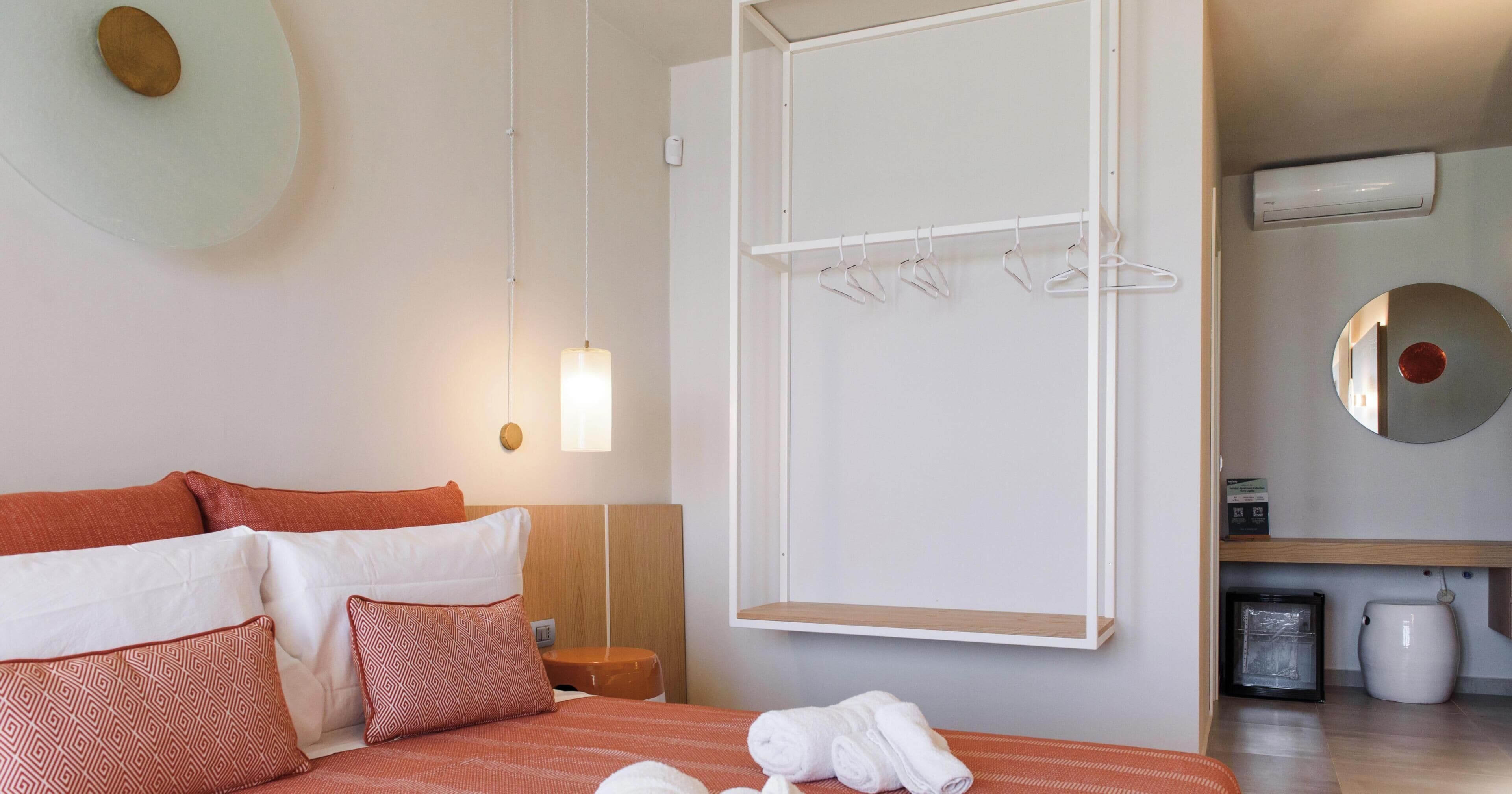 A hotel room with a bed, a hanging light fixture, a towel rack, and a mirror on the wall.