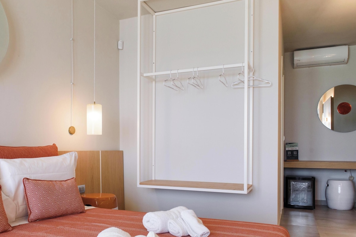 Een hotelkamer met een bed, een hanglamp, een handdoekhouder en een spiegel aan de muur.