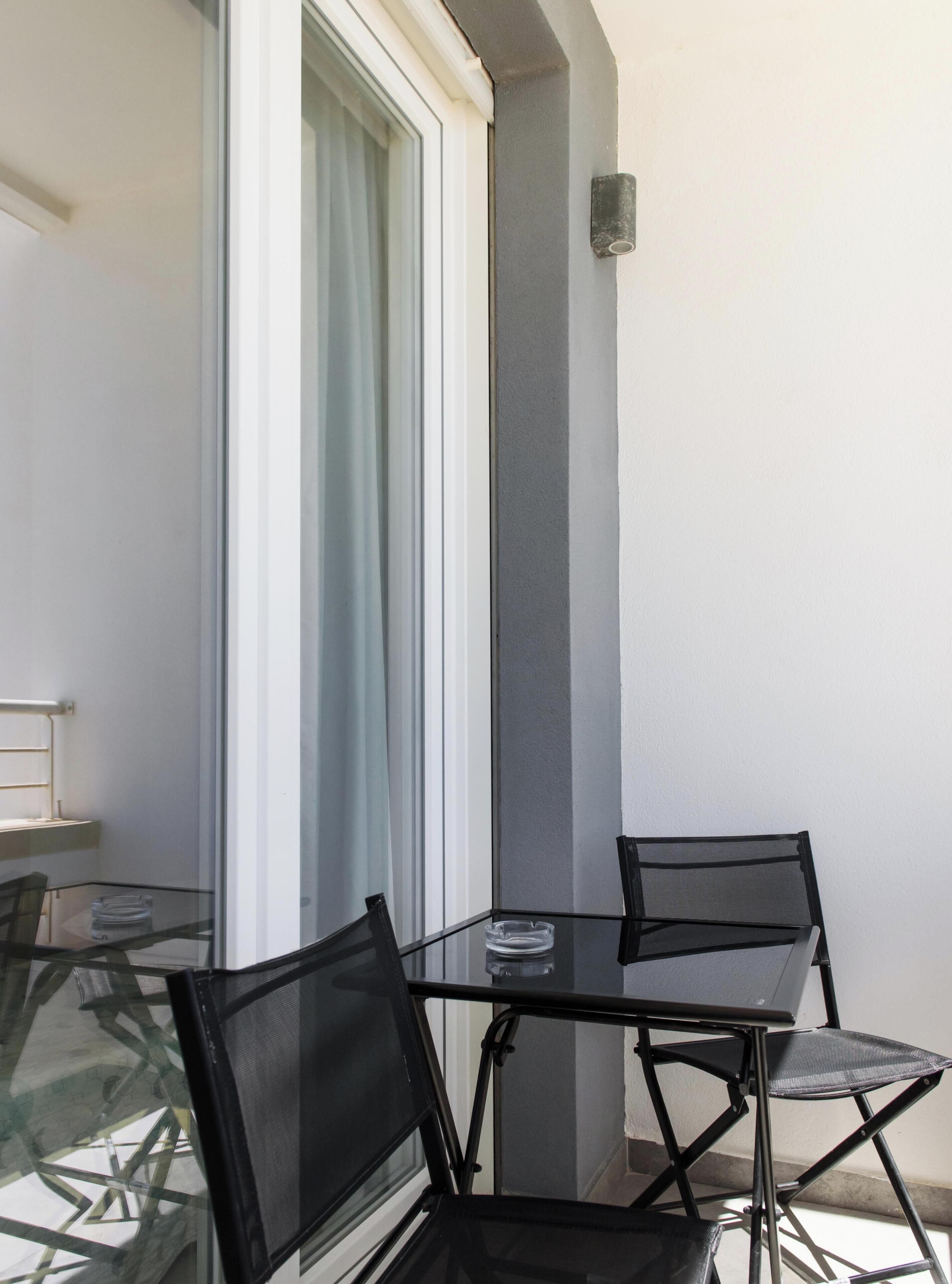 Ein Glastisch mit vier Stühlen, ein Fenster mit Vorhängen und einer Wandleuchte.